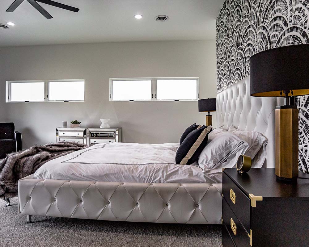 Modern luxury bedroom with tufted upholstered bed, black and gold accents, and dramatic patterned feature wall