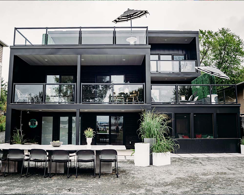 Modern black contemporary home exterior with multi-level balconies, outdoor dining area, and expansive glass railings