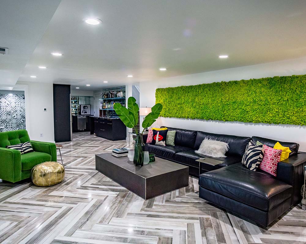 The updated lower level with green moss on the wall and a large black leather sectional