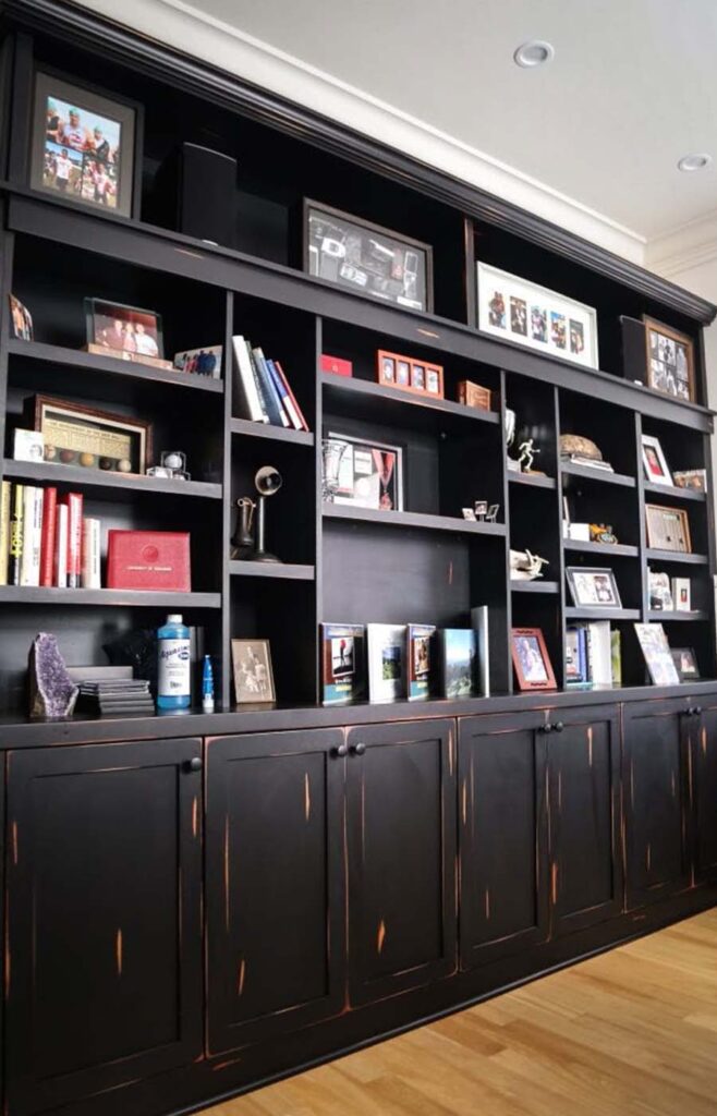 Custom black built-in shelving with books, framed photos, and decorative accents in modern home office interior