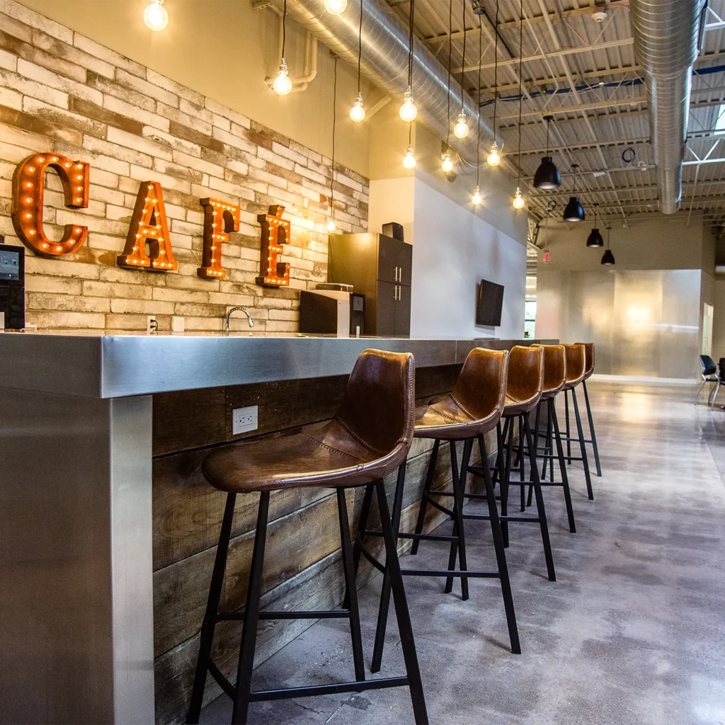 Industrial office café area with bar seating, exposed ductwork, and illuminated marquee wall sign