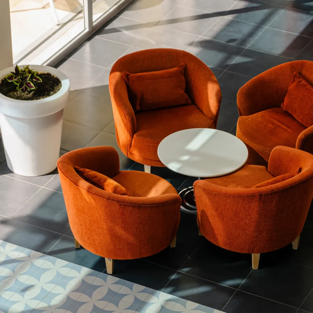Modern lounge seating area with orange accent chairs, round white table, and contemporary tile flooring