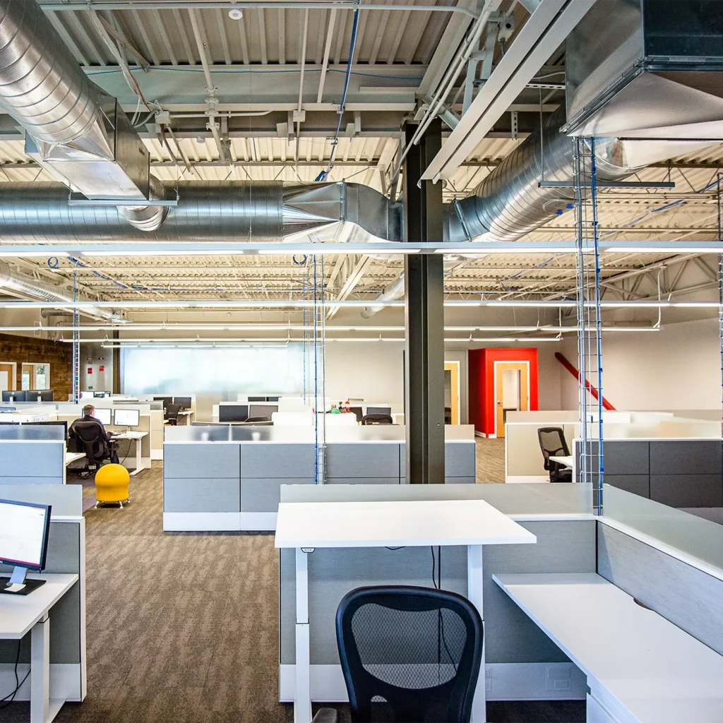 Modern open office workspace with exposed industrial ceiling and collaborative cubicle layout