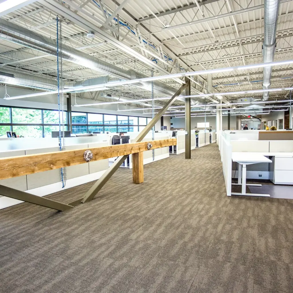 Modern open office workspace with exposed industrial ceiling, collaborative cubicles, and rustic beam accents