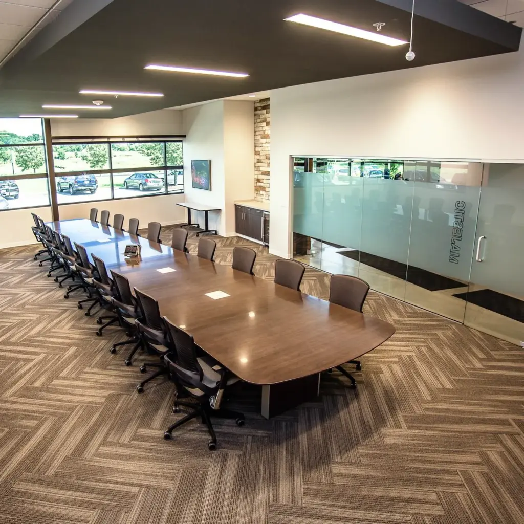Modern conference room with large wood meeting table, glass walls, and patterned commercial carpet flooring