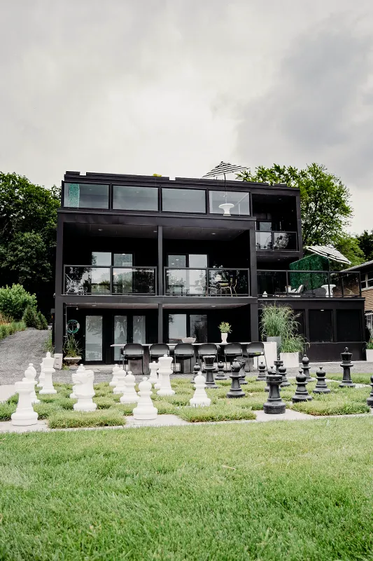 Modern black contemporary home exterior with outdoor chess set and landscaped lawn