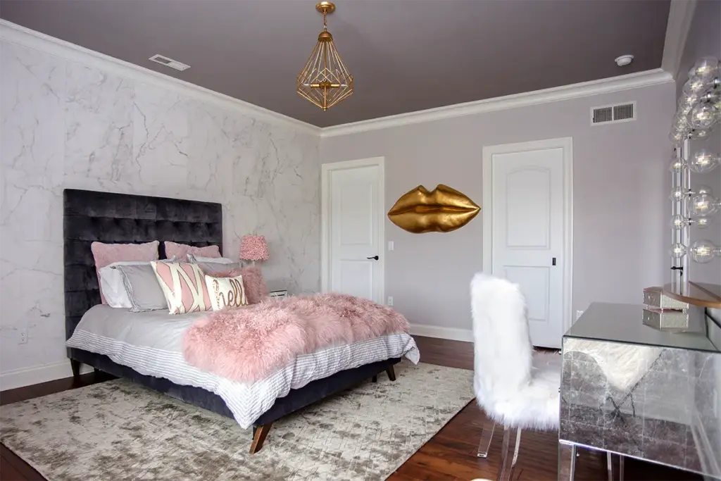 Modern glam bedroom with marble accent wall, blush pink bedding, and mirrored vanity decor